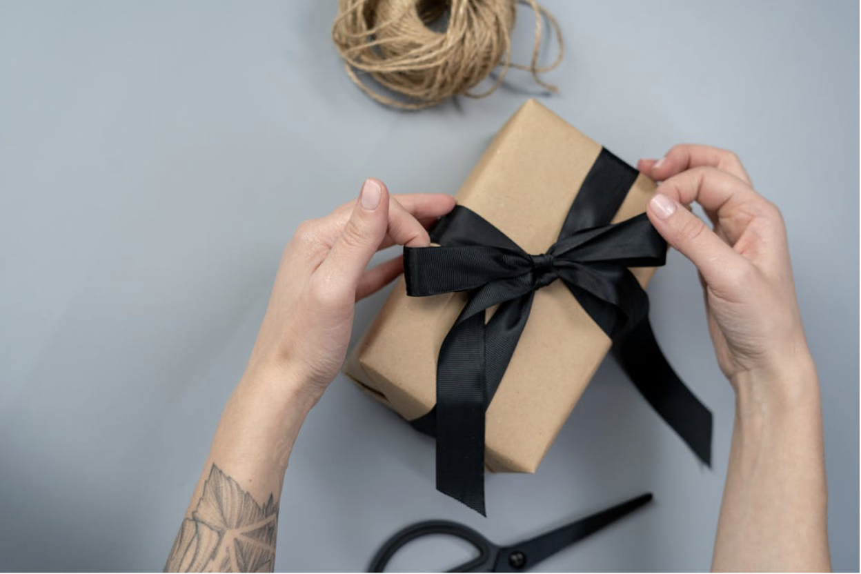 Hands wrapping a gift in beige paper with a black ribbon